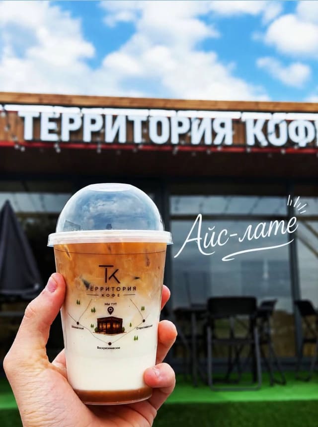 Айс-латте в фирменном стакане на фоне вывески «Территория кофе»